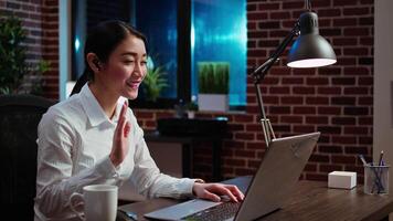 Smiling businesswoman saluting colleagues during company meeting on internet videocall in office. Employee speaking in remote videoconference telework call, brainstorming project ideas video