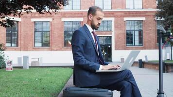 Man in suit sitting in business district working on the laptop. Next to his is an electric scooter video