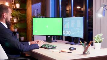 Manager in suit typing on computer with green screen in his office with moon light coming from window. video