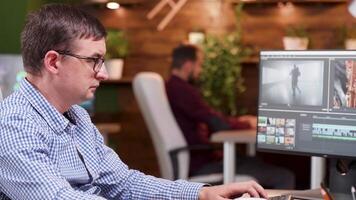 Video editor in the office taking a sip of coffee and working on video post production project.