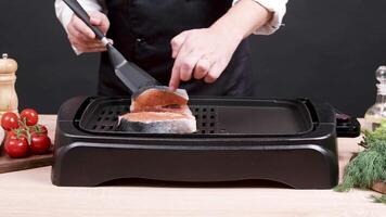 Chef preparing salmon seasoned with mediterranean herbs on electric pan. Roasted salmon. video