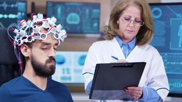 kvinna läkare tar anteckningar medan patient är bär hjärnor sensorer. medicinsk Centrum för hjärna forskning. video