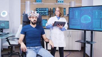 hembra médico comprobación el cerebro actividad de masculino paciente en un neurociencia instalación. hombre con onda cerebral exploración auriculares. video