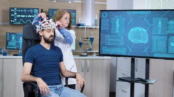 fêmea cientifico dentro pesquisa para cérebro atividade ajustando ondas cerebrais fone de ouvido em masculino paciente. video