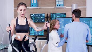 femmina medico nel sport scienza controllo il energia di femmina atleta su tv tenere sotto controllo. femmina atthele in esecuzione con elettrodi allegato per sua corpo. video