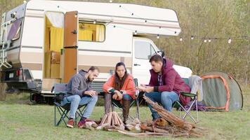 man talande en berättelse till hans vänner Sammanträde på camping stolar i främre av retro husbil skåpbil. video