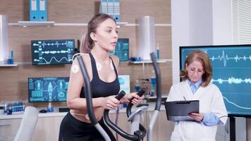 Female doctor mesuring the heart activity of female athlete. Female atthele running with electrodes attached to her body. video