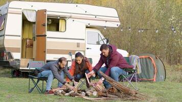 Friends setting up the wood for camp fire in front of retro camper van. Camping tent. video