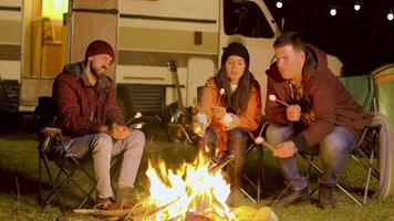 vänner avkopplande runt om läger brand och rostning marshmallows på pinnar. retro husbil skåpbil. kall natt. video