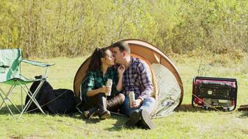 novio besos su Novia mejilla sentado en frente de su cámping carpa. Pareja relajante en desierto. generador. video