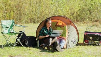 mooi jong vriendin lachend terwijl werken Aan haar laptop in camping tent. vriendje ontspannende terwijl vriendinnen werken. generator. video