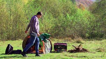 fidanzato seduta su campeggio posto a sedere mentre fidanzata preparazione il tenda per campeggio. giovane coppia nel il Di legno. video