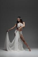 Belly and body of a woman dancing oriental dance in the studio, making beautiful body movements, she is dressed in a chic white suit on a dark background of the studio photo