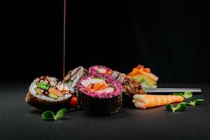 Various sushi, Japanese  lunch and side dishes and dipping teriyaki sauce on dark background. Side view of portion of Japanese sushi rolls set. Asian cuisine. Free space for your text photo