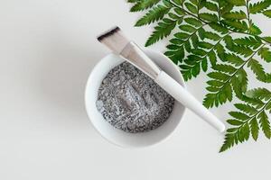 Preparing cosmetic mud mask in ceramic bowl on white background. Closeup texture of facial clay emulsion. Natural cosmetics for home or salon spa treatment photo