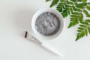 Preparing cosmetic mud mask in ceramic bowl on white background. Closeup texture of facial clay emulsion. Natural cosmetics for home or salon spa treatment photo