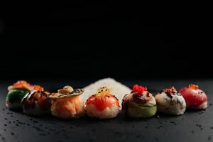 Sushi marco panorama, gastos generales plano laico disparo. rollos, maqui, nigiri en un negro pizarra fondo, japonés comida panorámico bandera. salmón, Anguila, camarón, atún con arroz, con Copiar espacio. alto calidad foto