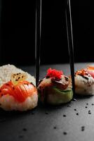 Sushi conjunto con caviar, aguacate y salmón. Sushi piezas metido Entre palillos, apartado en negro antecedentes. asiático cocina. parte superior vista. gratis espacio para tu texto. alto calidad foto