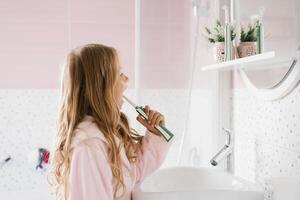 linda niña en un rosado bata de baño cepillos su dientes en un baño higiene concepto foto