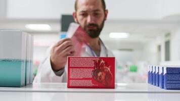 pov di Al dettaglio impiegato organizzazione medicamenti su farmacia scaffali, mettendo scatole di cardiologia i problemi pillole su Schermo. farmacista collocazione prescrizione farmaci e medicina nel negozio. tripode sparo. video