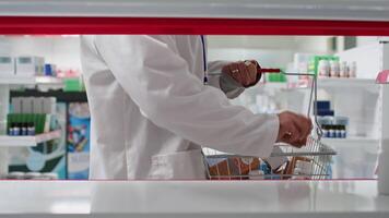 POV of medical employee placing all medicaments in boxes or bottles on display at drugstore, helping with products restock. Man working in a pharmacy, supplying shelves with medicine. Tripod shot. video