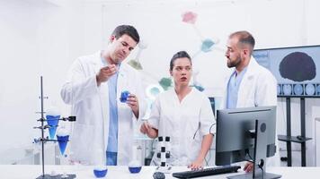 Group of three scientists in modern laboratory working with a blue smoking liquid. Science and research video