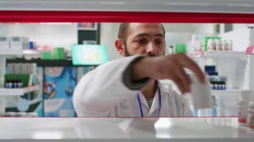 pov di Al dettaglio lavoratore organizzazione farmacia prodotti su scaffali, mettendo azione su Schermo per clienti per trova qualunque farmaco. farmacista Lavorando su organizzazione medicamenti nel farmacia. tripode sparo. video