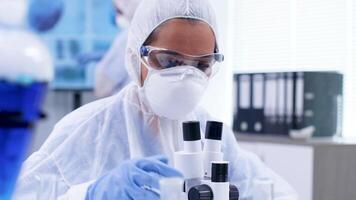 Close up footage of female scientist looking through moden microscope in research laboratory. Scientist in coverall protection equipment. video