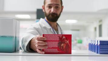 pov de employé vidange étagères dans local pharmacie, réorganiser médical des produits et soins de santé Provisions pour clients. Masculin boutique ouvrier prise des boites de drogues de pharmacie racks. trépied tir. video