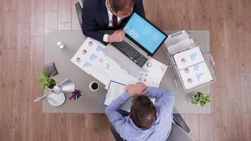 Top view of businessman in suit explaining charts from his laptop to new employee. video