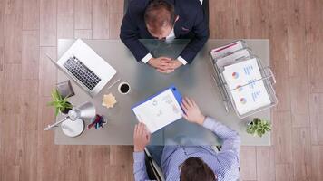 Top view of businessman in suit shaking hands with a manager and reading graphs form a clipboard. video