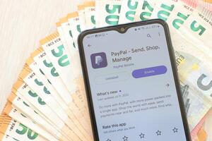TERNOPIL, UKRAINE - AUGUST 3, 2023 PayPal application on screen on modern smartphone and many bills of euro currency photo