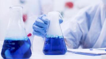 weiblich Wissenschaftler im ein Labor pflücken oben und halten ein Rauchen Blau Flüssigkeit im ein Flasche. Flüssigkeit Reaktion. video