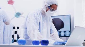 Female scientist in coverall equipment working on computer in a modern science laboratory. Scientist typing research raport on laptop. video