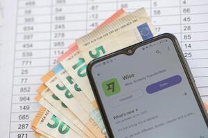 TERNOPIL, UKRAINE - AUGUST 3, 2023 Wise application on screen on modern smartphone and many bills of euro currency photo