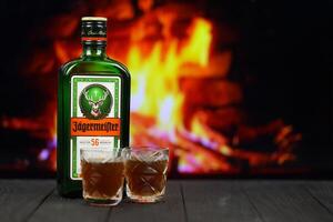 KYIV, UKRAINE - MAY 4, 2022 Jagermeister original alcohol bottle on wooden table with red fireplace photo