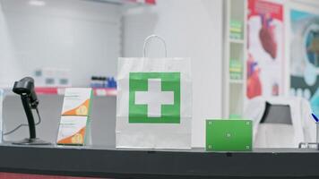 Paper bag with medicine and greenscreen surface shown on pills box at checkout counter, empty pharmacy having medicaments and vitamins at cash register. Nutrients and chromakey copyspace layout. video