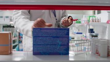 pov do farmacêutico colocando produtos a partir de prateleiras dentro a cesta, reorganizando medicamentos Sediada em tipos e usa. cuidados de saúde trabalhador levando fora caixas do produtos farmacêuticos a partir de prateleiras. tripé tomada. video