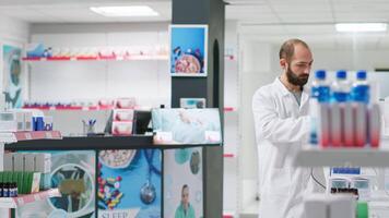 farmacéutico exploración médico productos cajas en cuidado de la salud almacenar, trabajando en comprobación medicamentos valores en vacío farmacia. empleado utilizando escáner en tableta a hacer farmacéutico inventario. video