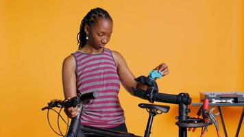 BIPOC mechanic setting up bike repair stand, using it to adjust handlebar and fix broken wheels, studio background. Professional placing bicycle on workstand in tight grip to inspect it, camera B video