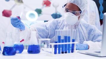 Female scientist in protection gear using a pipette to take a sample of smoking blue fluid. Test tubes with blue solution. video