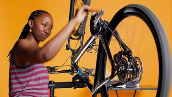 bipoc Ingenieur Überprüfung Fahrrad Performance durch Spinnen Pedale. erfahren Spezialist gewährleisten richtig Funktion von Reifen auf Fahrrad Räder im Orange Studio Hintergrund während Wartung, Kamera b video