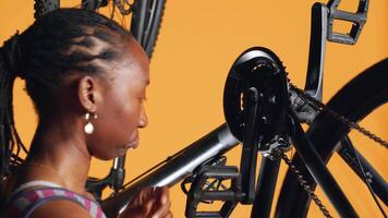 afrikansk amerikan kvinna tryckande pedaler till snurra cykel hjul, inspekterande Det, använder sig av skruvmejsel och hex uttag rycka till fixera Det, stänga upp skott. ridning hobbyist testning cykel vev ärm och kedja ringar video