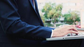 Manger in business suit typing on laptop keyboard outdoor in the city, close up video