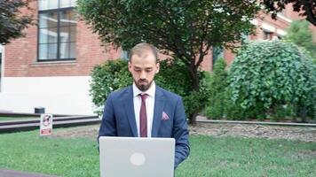 gerente en formal traje mecanografía en el computadora portátil, trabajando al aire libre en el ciudad. negocio en el Vamos video