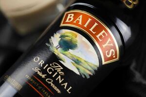 KYIV, UKRAINE - MAY 4, 2022 Baileys original alcohol bottle on wooden table with black fabric photo