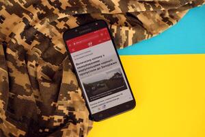 KYIV, UKRAINE - 4 MAY, 2023 24tv ukrainian news portal on smartphone screen with ukrainian flag and camouflage fabric photo