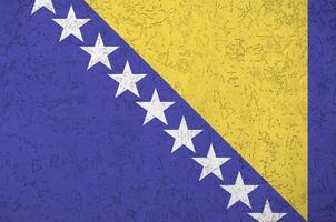 Bosnia and Herzegovina flag depicted in bright paint colors on old relief plastering wall. Textured banner on rough background photo