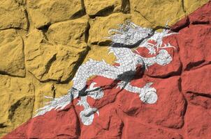 Bhutan flag depicted in paint colors on old stone wall closeup. Textured banner on rock wall background photo