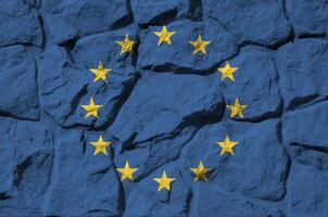 European union flag depicted in paint colors on old stone wall closeup. Textured banner on rock wall background photo